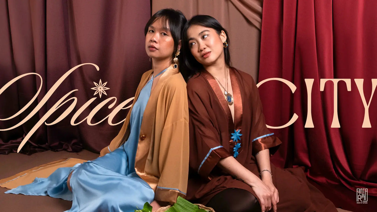 Spice City collection: two models in silk robes in caramel, blue and rust, seated before red curtains